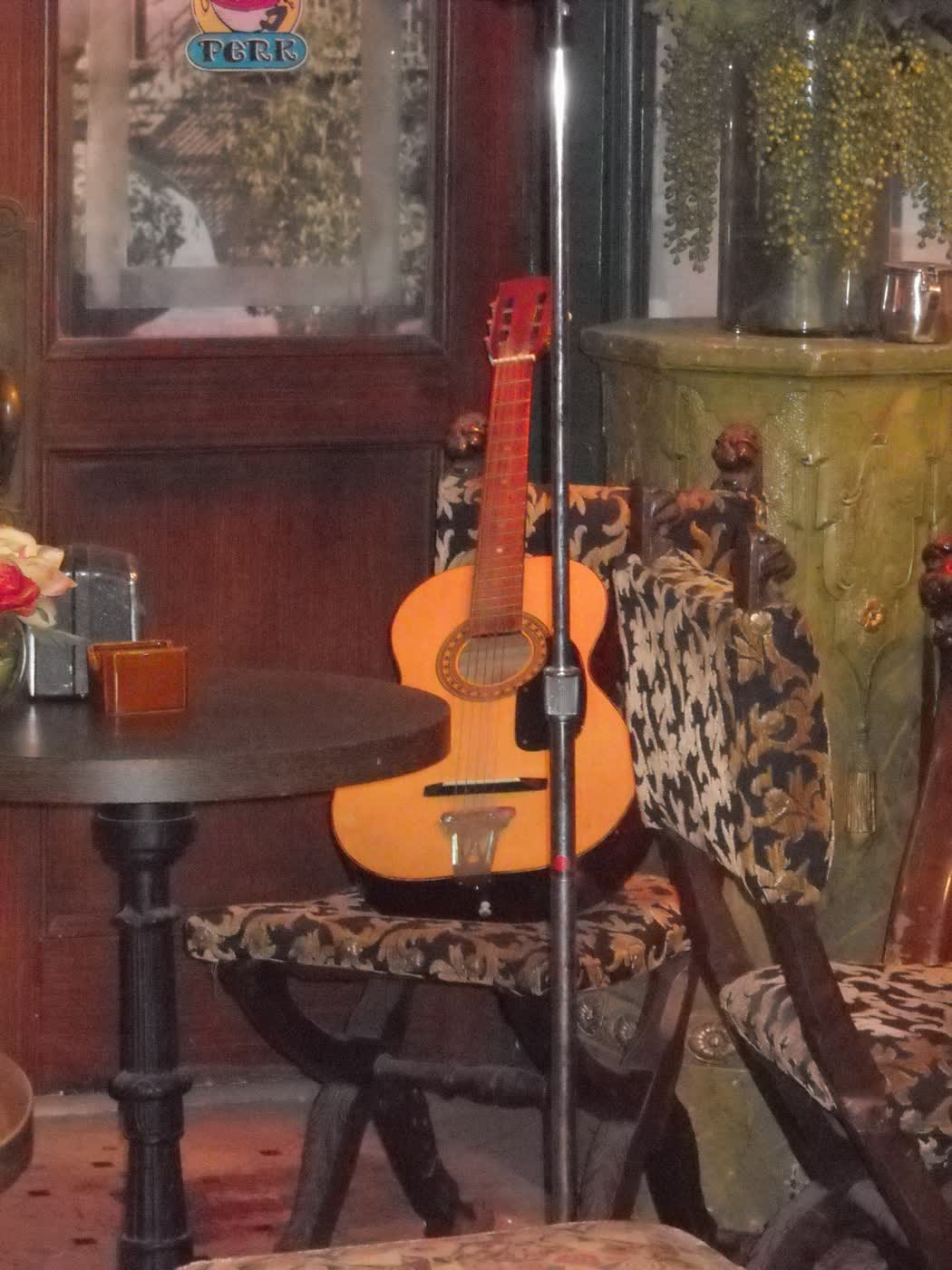 An acoustic guitar on a stand beside a leopard-print chair at Central Perk